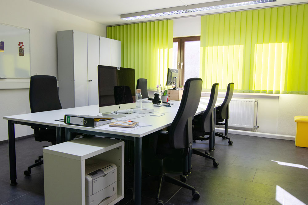 Büro mit drei Stühlen, Drucker und Schrank. Im Hintergrund grüne Vorhänge